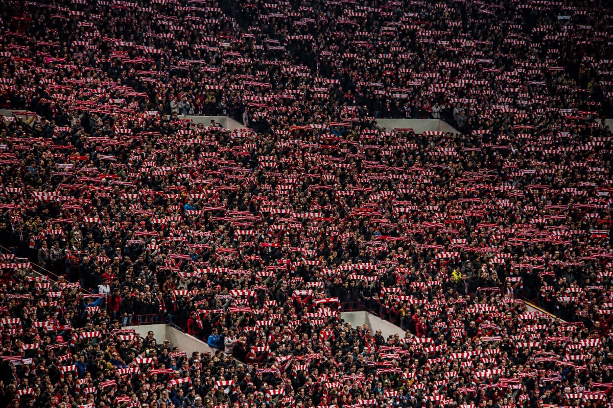 A matchday crowd of supporters holding scarves aloft